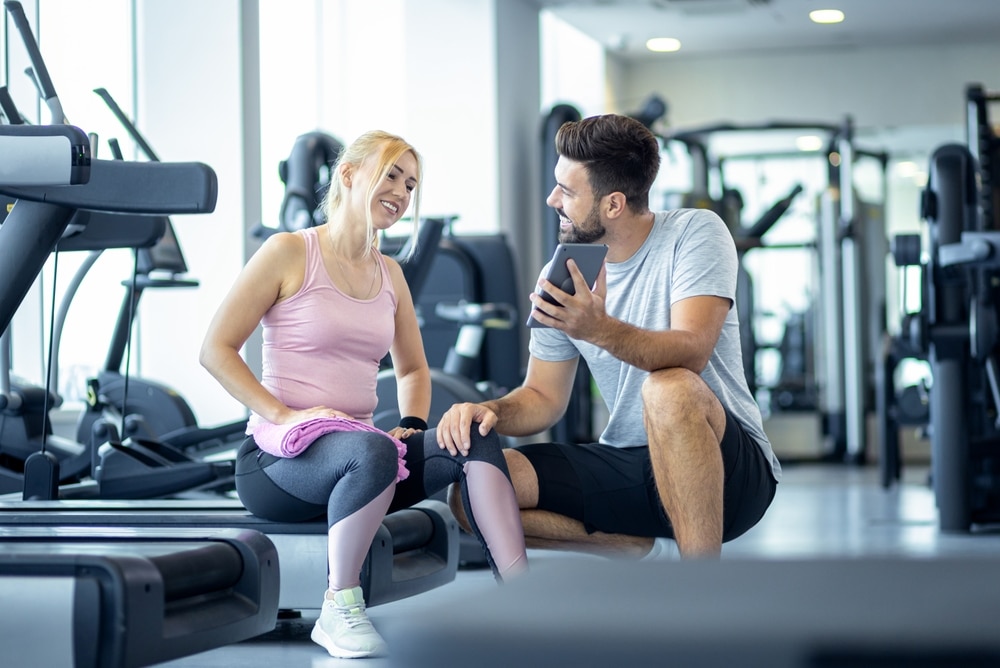 Personal trainer ja asiakas keskustelevat rennosti puhelimen ääressä kuntosalilla
