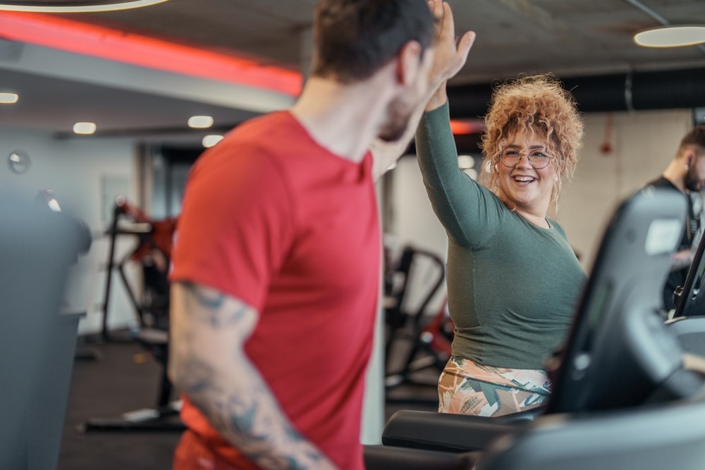 Asiakas ja personal trainer juhlistavat onnistunutta harjoitusta yläfemmalla juoksumatolla